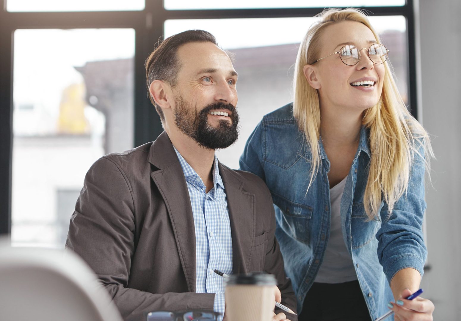 Two business partners look attentively at presentation of full screen, being glad meet together, focused into distance, going to have coffee break. Creative copywriters collaborate for common project